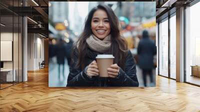 A woman's bright smile is framed by her winter attire as she enjoys coffee at a bustling street market, embodying warmth and the joy of urban exploration. Wall mural