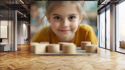 A young girl with a joyful expression focuses on building wooden blocks in a classroom, capturing the essence of playful learning and creativity among children. Wall mural