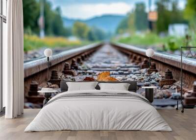 Close-up of a single leaf resting on railway tracks, with a perspective view extending into a distant landscape featuring trees and hills under a cloudy sky. Wall mural