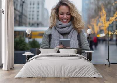 In a busy city center, a woman in a warm scarf enjoys using her smartphone amidst twinkling holiday lights and a bustling urban winter atmosphere. Wall mural