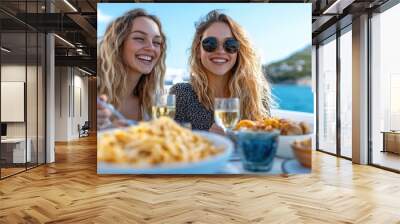 Two women smile brightly as they enjoy pasta and wine on a boat surrounded by beautiful scenery, capturing a moment of joy, celebration, and good company. Wall mural