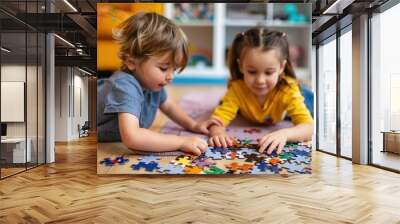 Two young children, a boy and a girl, are lying on the floor indoors solving a puzzle together, depicting a moment of teamwork, concentration, and playful learning in a cozy setting. Wall mural