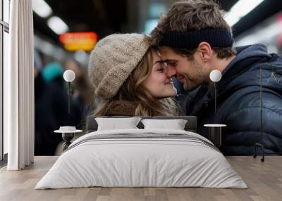 Wrapped warmly in winter clothing, a couple enjoys a moment of happiness as they lean in towards each other in a bustling subway station setting. Wall mural