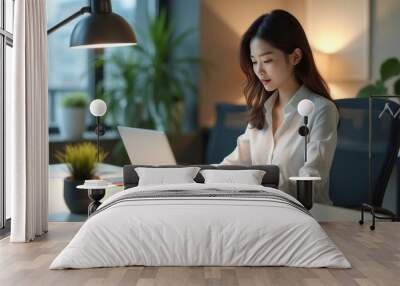 Focused professional woman working on a laptop at a modern office desk with evening lighting and a serene atmosphere. Wall mural