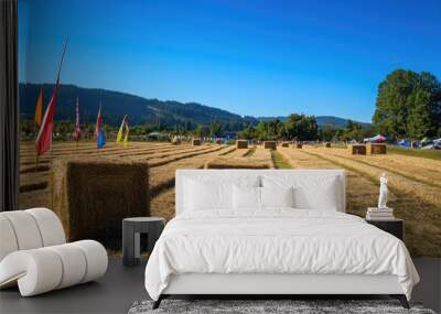 A hay bale maze set up in a field for a seasonal festival, with colorful flags and a clear blue sky overhead. Wall mural