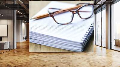 A stack of lined notebook paper sheets with a pencil and a pair of reading glasses resting on top Wall mural