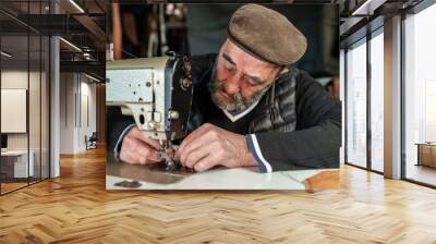 Old hipster bearded man with flat cap setting a sewing machine. Craftsmanship concept. Wall mural