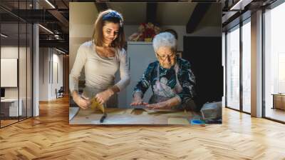 Portrait of caucasian grandmother and granddaughter smiling preparing dough for making fresh homemade pasta. Spending time together in family. Traditional Italian food.  Wall mural