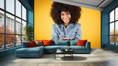 Half body picture of young crazy excited happy african woman playing video game sitting on armchair isolated on yellow color Wall mural