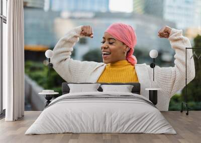 Latina woman, fighting breast cancer, wears a pink scarf, and clenches her arms as a survivor fighter Wall mural