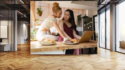 lesbian women couple in the kitchen at home with computer, multiracial women who love each other and live together. Wall mural