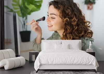 pretty woman with curly hair putting on makeup at home with a brush Wall mural