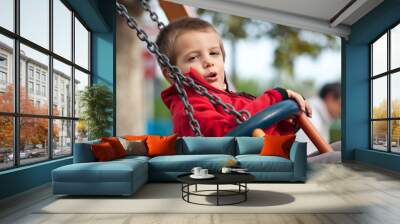 3 year old kid swinging on a sunny day with trees in the backgro Wall mural