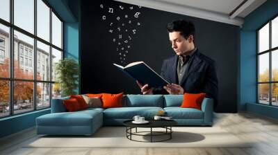 young man reading book with letters coming out. Wall mural