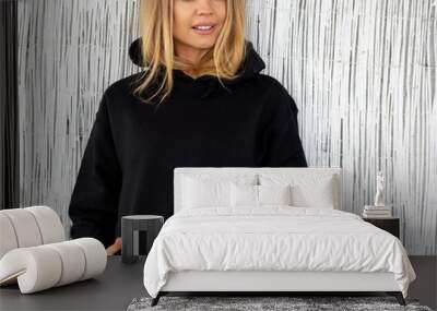 Sweatshirt hoodie mockup. A nice smiling blonde poses in a black sweatshirt against a white wall. She is sitting facing the camera. Wall mural