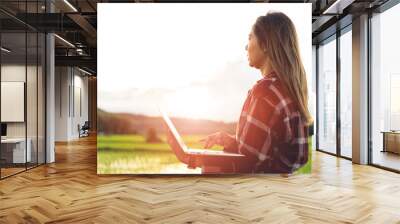 Asian woman farmer using laptop to store farm data In the evening with warm light. Agricultural technology concept. Organic agriculture. Wall mural