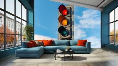 An English traffic light sits isolated against a bright blue sky with the red, orange and green lights Wall mural