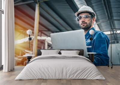 Confident engineer in blue jumpsuit holding laptop computer in a warehouse. Wall mural