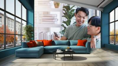 Gay asian couple looking at smartphone together indoors. Wall mural