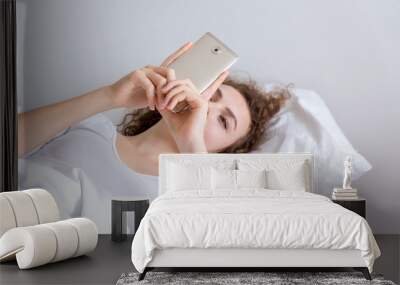 Young woman getting tired from looking at phone on the bed. Wall mural