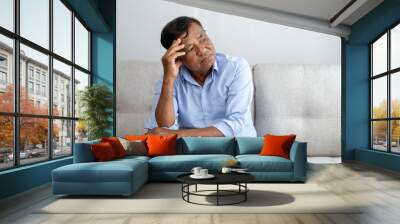 Asian retired elderly thinking and looking away sitting on the sofa alone at home, feeling sad or worried Wall mural