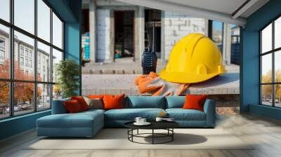 Yellow safety helmet, gloves and walkie talkie at construction site against background. Wall mural