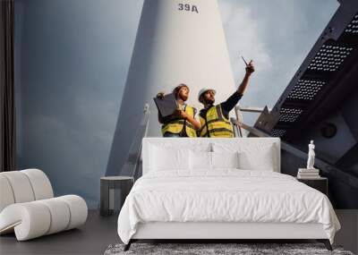 Young man and woman maintenance engineer team working and holding the report in wind turbine farm. Generator station, renewable energy Wall mural