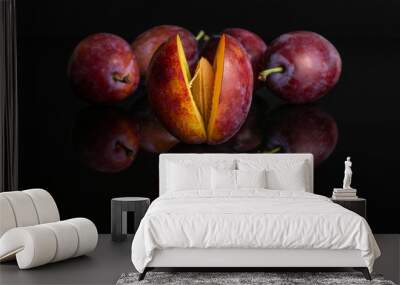 Group of five whole fresh blue plum one is in the front halfway open with a stone isolated on black glass Wall mural