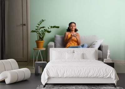 African-American teenage girl drinking tea while sitting on sofa at home Wall mural