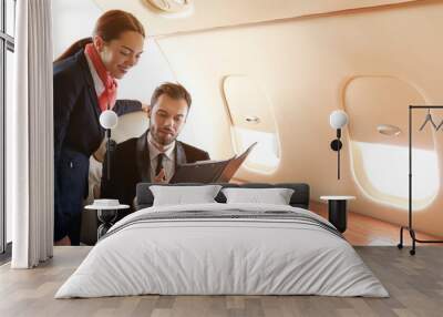 Air hostess showing menu to businessman on board the modern private airplane Wall mural