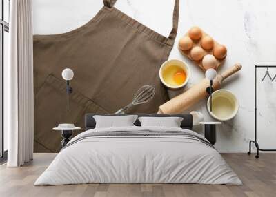 Apron, kitchen utensils and eggs on light background Wall mural