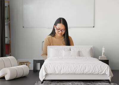 Asian female teacher sitting at table in classroom Wall mural