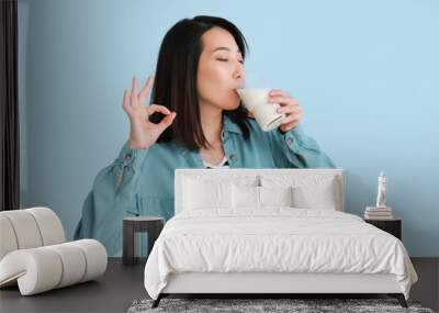 Beautiful Asian woman drinking milk and showing OK on light blue background Wall mural