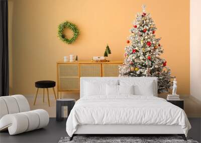 Beautiful Christmas tree with gift boxes and chest of drawers near beige wall Wall mural