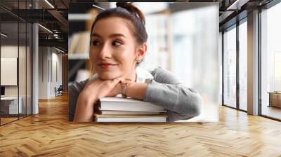 Beautiful female student with stack of books in library Wall mural