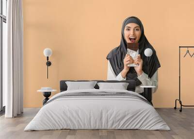 Beautiful Muslim woman eating tasty chocolate on color background Wall mural