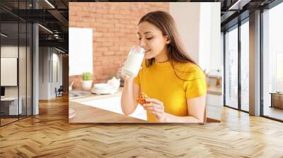 Beautiful woman drinking tasty milk with cookies in kitchen at home Wall mural