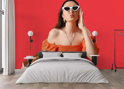 Beautiful woman in sunglasses with box of tasty pizza blowing kiss on red background Wall mural