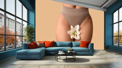 Beautiful young African-American woman in panties with white lily flower on beige background, closeup Wall mural