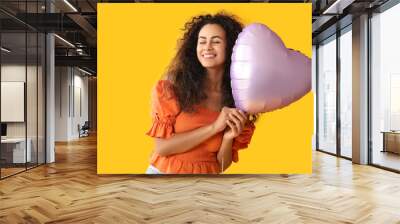 Beautiful young African-American woman with heart shaped air balloon on yellow background Wall mural