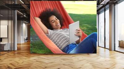 Beautiful young African-American woman with tablet computer resting in hammock outdoors Wall mural