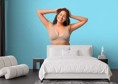 Beautiful young happy African-American body positive woman in tight jeans on blue background Wall mural