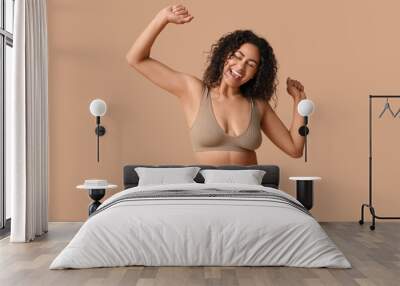 Beautiful young happy African-American woman in underwear dancing on beige background Wall mural