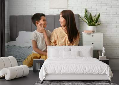 Beautiful young happy Asian mother with cute little son sitting in bedroom at home Wall mural