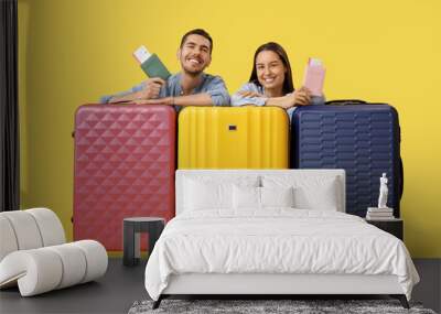 Beautiful young happy couple of tourists with passports, tickets and suitcases on yellow background Wall mural