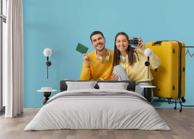 Beautiful young happy couple of tourists with suitcase, passport and camera sitting on blue background Wall mural