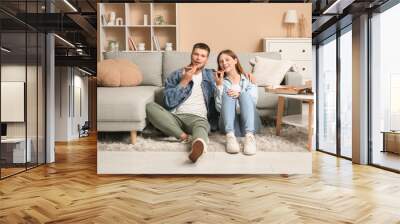 Beautiful young happy couple with pieces of tasty pizza sitting on floor at home Wall mural