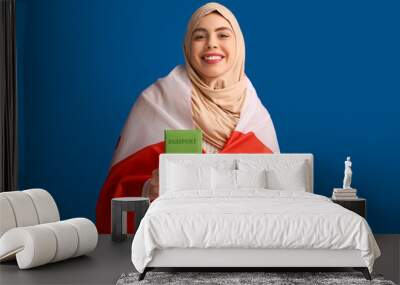 Beautiful young happy Muslim woman with Canadian flag and passport on blue background Wall mural