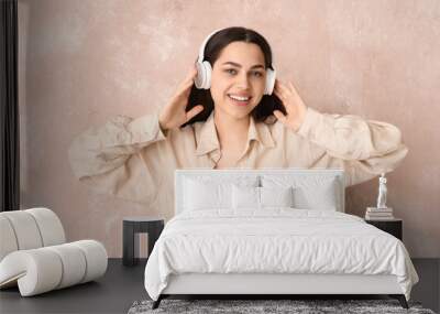 Beautiful young happy woman in headphones listening music on beige grunge background Wall mural