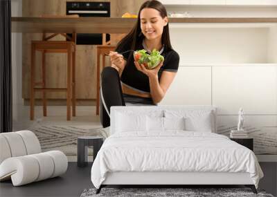 Beautiful young happy woman with bowl of fresh salad sitting in kitchen at home. Weight loss concept Wall mural